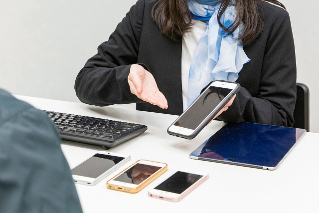 4台のスマートフォンをそれぞれ説明する女性販売員
