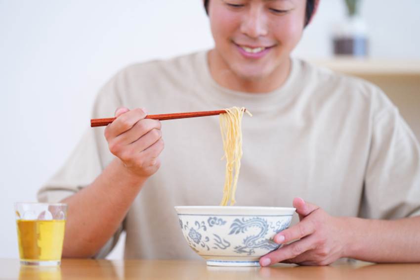 笑顔で麺類を食べる男性