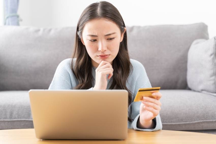 パソコンの前で、クレジットカードを、かをしかめながら見る女性
