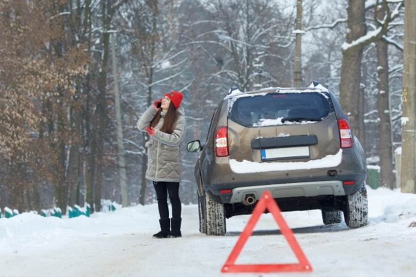 雪が積もっている山林の中で、ロードサービスに連絡をしている女性