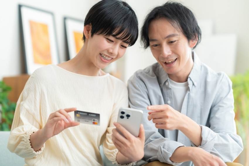 クレジットカードとスマートフォンを見る夫婦