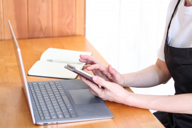 PCの情報を見ながらスマートフォンを操作する女性