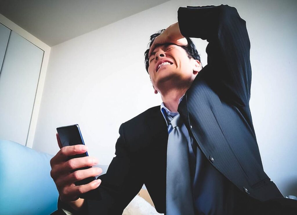 スマートフォンを握りながら、左手で頭を抱える男性
