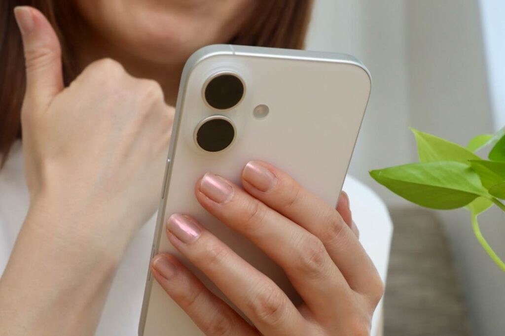 スマートフォンの画面を見ながら、右手の親指を立てる女性